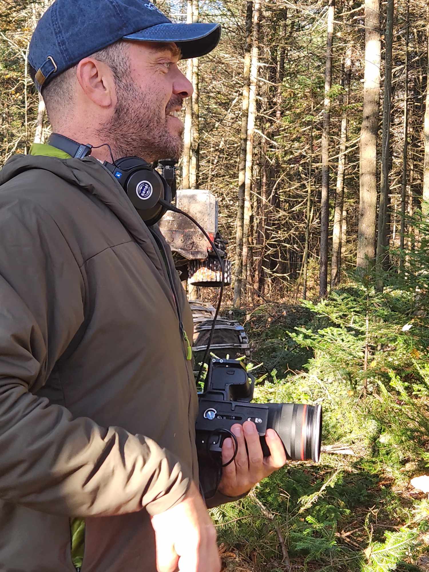 Charles filming in forest wearing olive jacket and blue cap